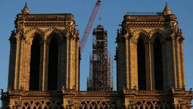 เครนกำลังวางประติมากรรมรูปไก่สีทอง ซึ่งเป็นกังหันชี้ทิศทางลม บนยอดแหลมของอาสนวิหารแห่งนี้ที่ยังอยู่ระหว่างการซ่อมแซม