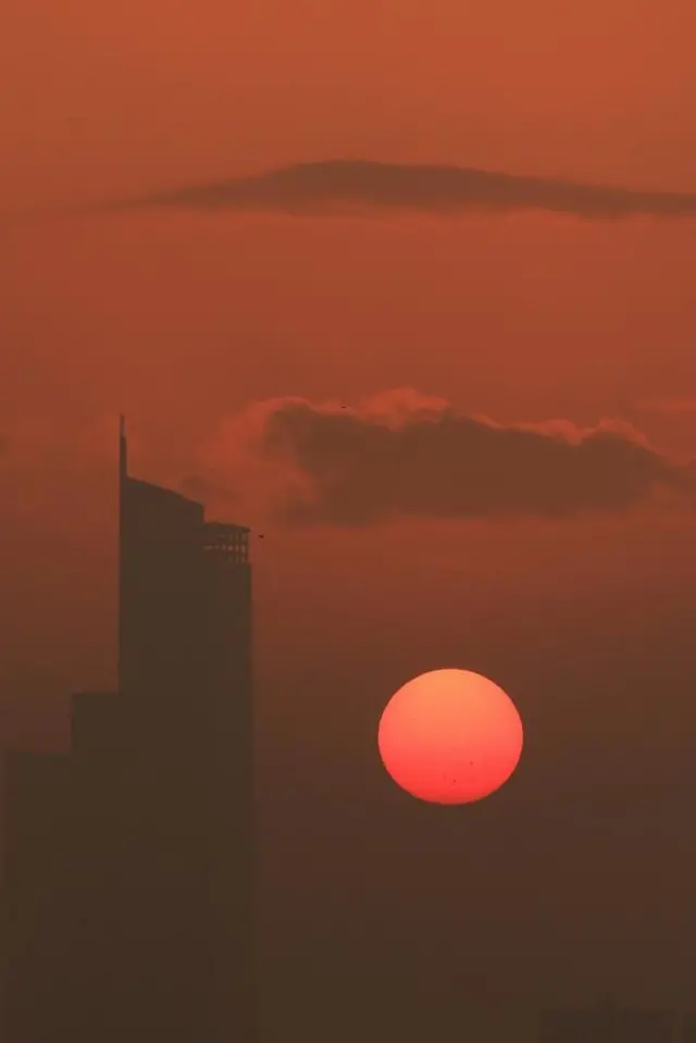 高層ビルのシルエットの横に、赤い太陽が上がり、空を茜色に染めている