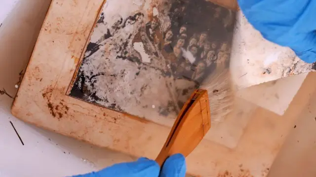 Una fotografía dañada en blanco y negro que está siendo limpiada por una brocha.