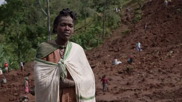 Wata mace ta na kallon mai daukar hoto, a bayan ta mutanen da suka tsira daga zabtarewar kasar da ta faru a Gofa ne, ranar 25 Yuli 2024