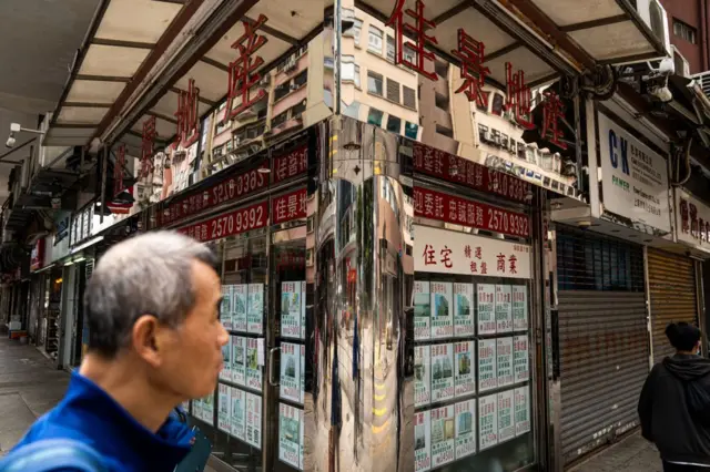 一名白頭髮的男子在地產鋪門外。