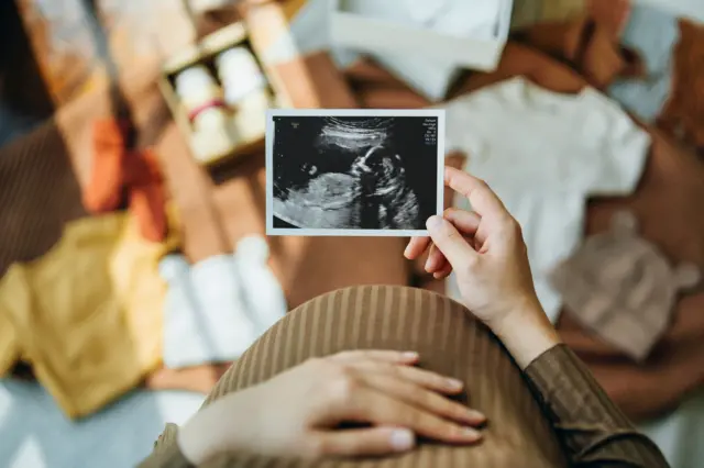 Mulher grávida com mão na barriga segura foto de ultrassom