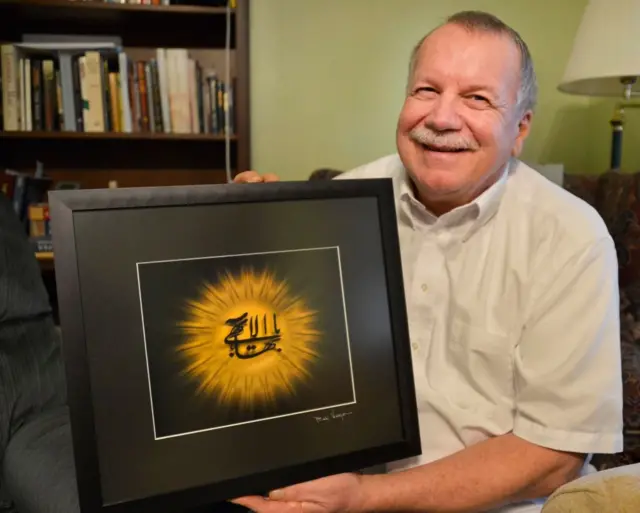 يحمل الأمريكي بول موراي رمزًا للدين البهائي، وهو عبارة عن رسم بالخط العربي مؤطر يُعرف باسم "الاسم الأعظم" في منزله في مدينة ألباني الأمريكية، صورة تعود لعام 2013