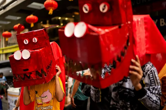 Дети в масках в виде драконьих голов, сделанных из коробок и покрашенных в красный цвет.