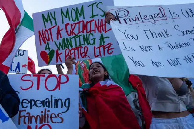 Uma jovem com uma bandeira do México e um cartaz em inglês que diz: "Minha mãe não é uma criminosa por querer uma vida melhor"