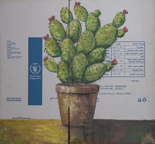 رسم على اللوحة نبتة صبار ملونة بالأخضر في وعاء مخصص للزراعة لونه بني على كرتونة مساعدات.