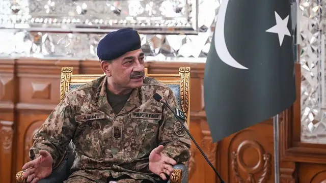 عاصم منیر روی صندلی نشسته درحال صحبت است، پرچم پاکستان در کنار اوست