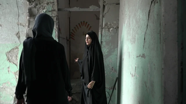 Amaineh Nademi, Minab'daki Shajareh Tayyebeh İlkokulu'nun kalan koridorlarından birinde yürüyor. Siyah bir çarşaf giyen Nademi, BBC muhabiri Nawal Al-Maghafi'ye okulun hasarını gösteriyor. Beton duvarlar çatlamış ve daha önce açık yeşil renge boyanmıştı.