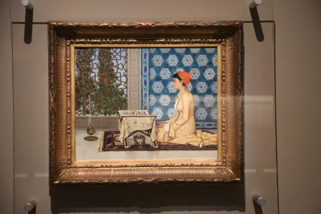 Osman Hamdi Bey'in Genç Kadın Okurken adlı eseri bir camın arkasında duvarda asılı bir şekilde