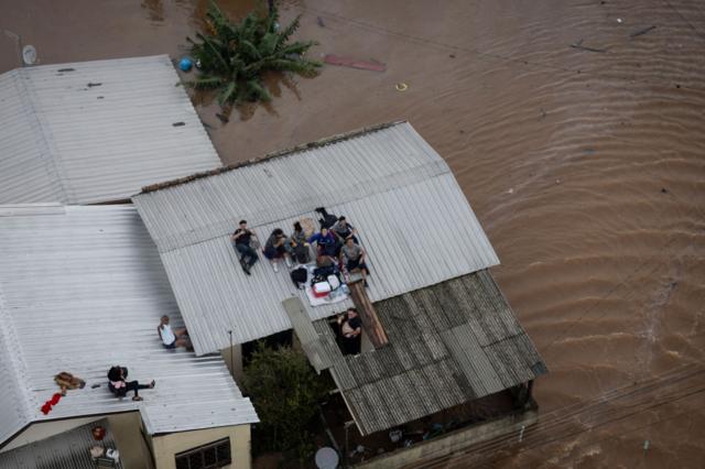 Pessoas em cima de telhado aguardando para serem resgatadas