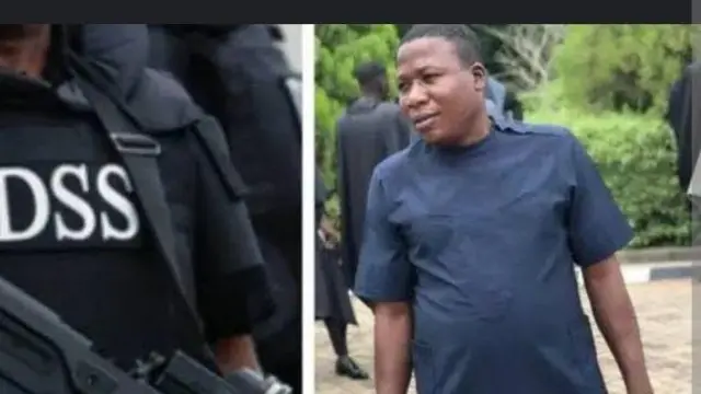 Sunday Igboho nínú aṣọ aláwọ̀ búlúù dúró lẹgbẹ ọtun, àwòrán ìdámọ̀ iléeṣẹ́ Otelemuye DSS wa lápá òsì