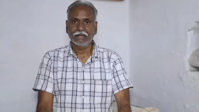 Avadhiya's son Neeraj wearing a white check shirt. His hairs have turned white and is wearing a chain 