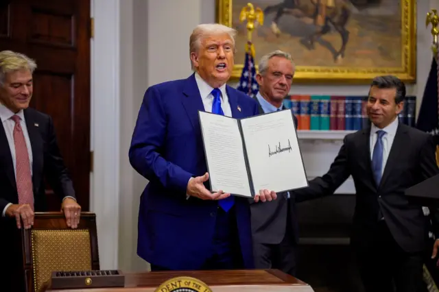 Donald Trump holds up a signed paper, flanked by Mehmet Oz, Robert F Kennedy Jr and Martin Makary