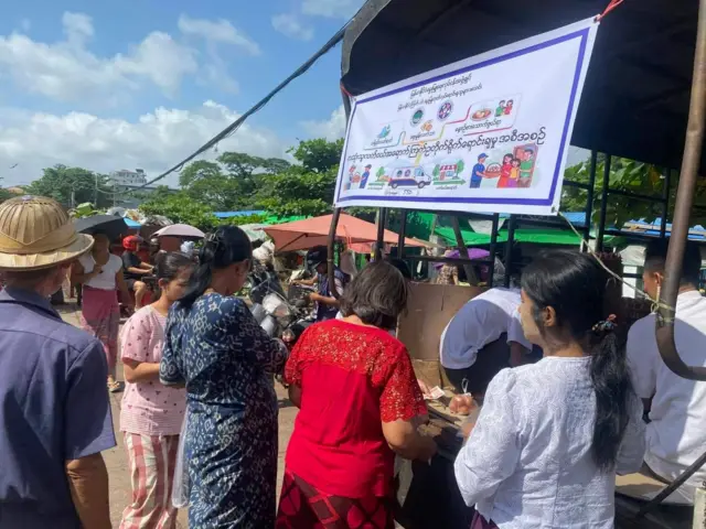 ကြက်ဥတိုက်ရိုက်ရောင်းချတဲ့အစီအစဥ်ဗီနိုင်းစာရွက်ချိတ်ထားတဲ့ ကားနောက်ခန်းမှာ တန်းစီရပ်ပြီး ကြက်ဥဝယ်နေသူတွေ 
