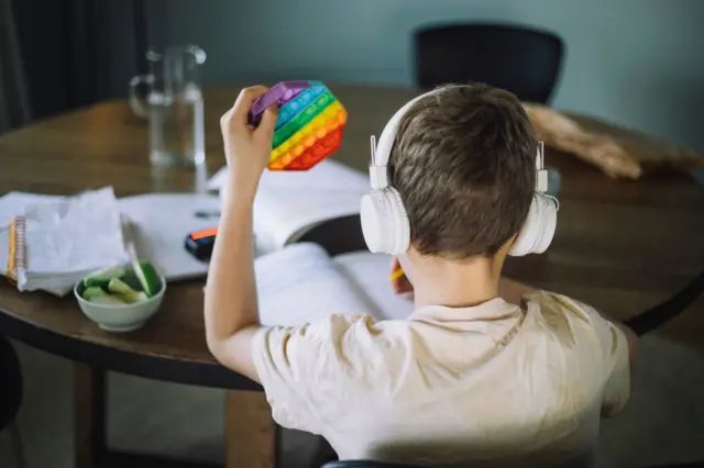 Criança faz lição com fone de ouvido e brinquedo para concentração