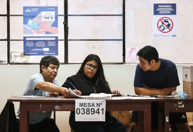 Tres personas tras una mesa electoral en un centro de votación de Lima. 