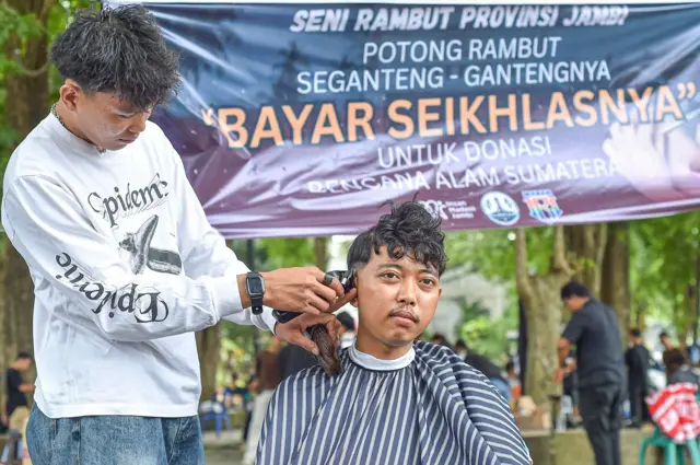 Kapster dari Seni Rambut Provinsi Jambi memangkas rambut warga saat penggalangan dana melalui aksi pangkas rambut bayar seikhlasnya di Taman Banjuran Budayo, Kota Baru, Jambi, Minggu (21/12/2025). 