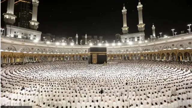 Akojọpọ awọn eeyan to n ṣiṣẹ Hajj ni Saudi, wọn lọ aṣọ funfun mọra, to lobiripo nibi ina alaranbara to rẹwa yika. Kaaba wa niwaju wọn.