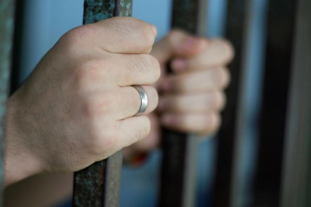 Mãos de pessoa nas grades da prisão
