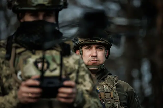 Drone kullanan Ukraynalı iki asker görüyoruz. Birinin elinde uzaktan kumanda aleti var.