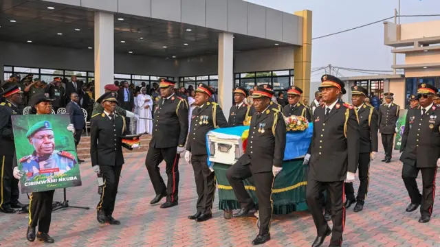 Abasirikare baherekeje isanduku y'abapfuye iriho indabo n'ibendera ry'igihugu n'undi uri imbere afite ifoto nini iriho Jenerali Peter Cirimwami mu muhango wo kumusezeraho