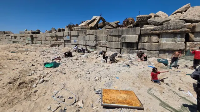 أشخاص بينهم أطفال يبحثون ويجمعون قطع الاسمنت من ميناء غزة
