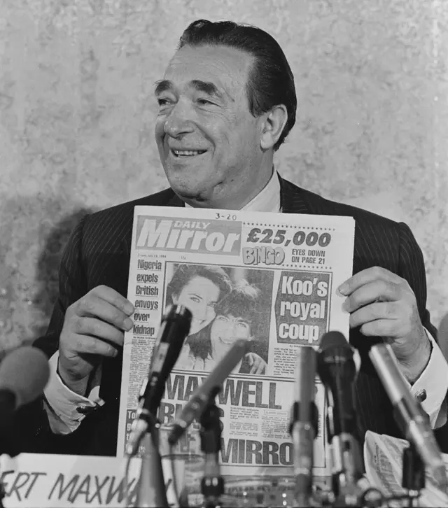 Maxwell en conferencia de prensa sosteniendo el diario y sonriendo