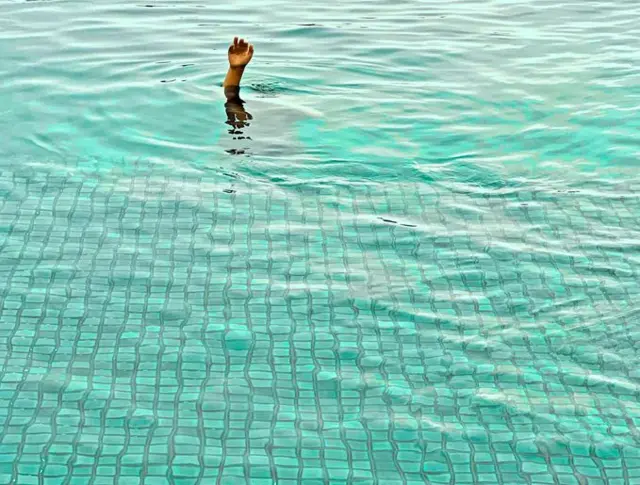 a stock photo, showing a hand reaching out of a swimming pool