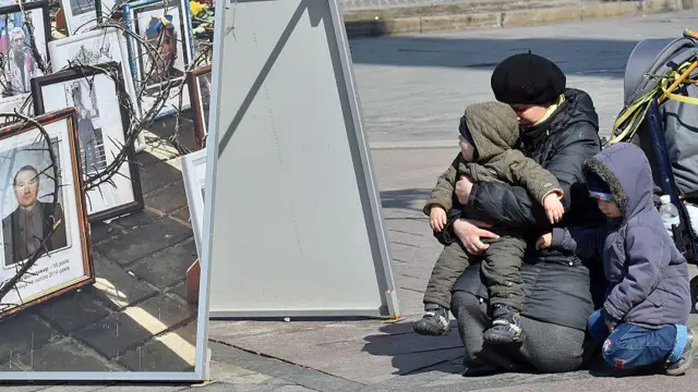 Жінка стоїть на колінах зі своїми дітьми під час похоронної церемонії 