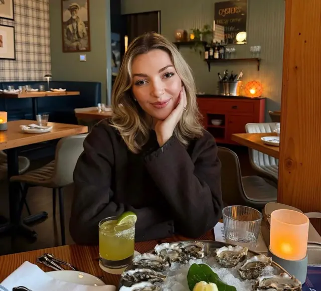 Ginger Smith se senta à mesa de um restaurante, com um coquetel e um prato de ostras