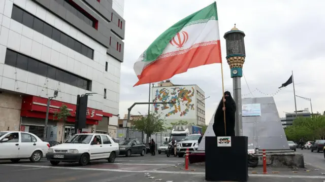 Женщина держит иранский флаг на улице в Тегеране, Иран, 12 апреля 2026 года.