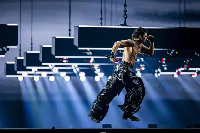 Мушкарац го до појаса трчи на сцени у кожним панталонама