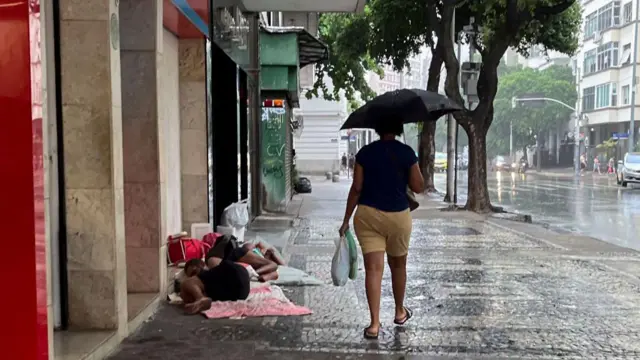Uma mulher se abriga sob um guarda-chuva enquanto passa por moradores de rua durante um dia chuvoso no Rio de Janeiro, em 22 de março de 2024.