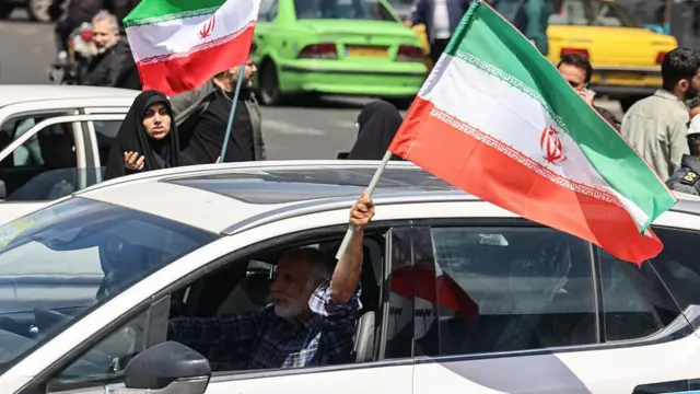Мужчина размахивает иранским флагом, сидя в машине на площади Революции в Тегеране