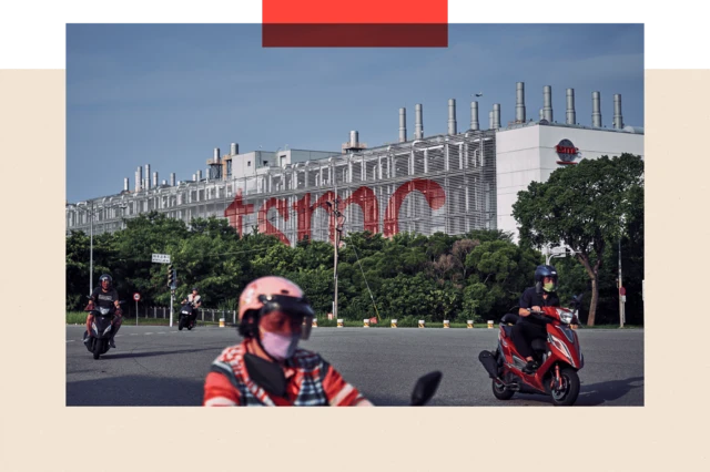 Una planta de TSMC en Taiwán. Es un edificio horizontal plateado con las letras TSMC en rojo. Frente a él pasan motos que conducen personas con mascarillas.  