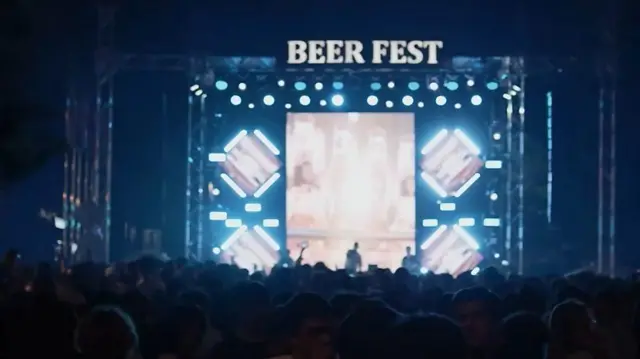 Qorong‘i payti, festivalda sahnada bir kishi qo‘shiq aytyapti, tomoshobinlar qo‘llarida telefon bilan rasmga olyapti.