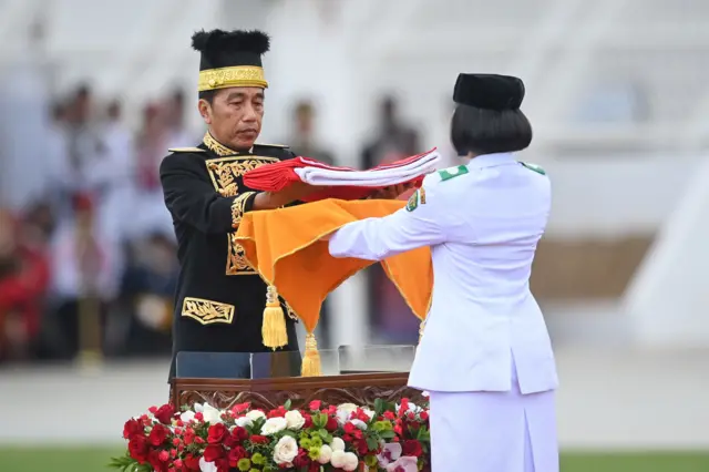Presiden Joko Widodo (kiri) menyerahkan duplikat Bendera Pusaka kepada anggota Paskibraka 2024 asal Kalimantan Timur Livenia Evelyn Kurniawan (kanan) untuk dikibarkan dalam upacara Peringatan Detik-detik Proklamasi Kemerdekaan Republik Indonesia (RI) di lapangan upacara Istana Negara Ibu Kota Nusantara (IKN), Penajam Paser Utara, Kalimantan Timur, Sabtu (17/8/2024).