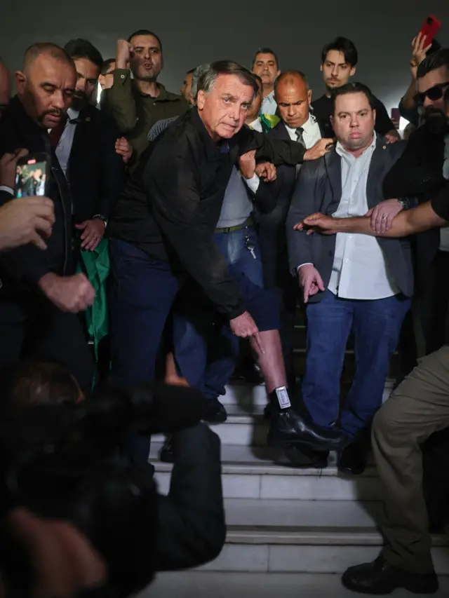 Jair Bolsonaro cercado de apoiadores, mostrando sua tornozeleira eletrônica em 21 de julho de 2025