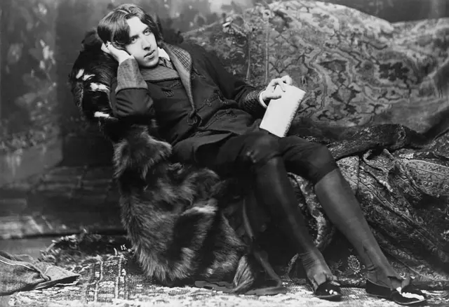 Foto em preto e branco de Oscar Wilde recostado num sofá coberto com uma estola de pele