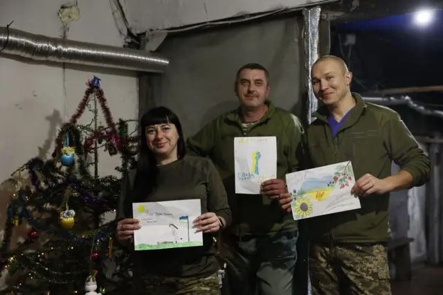 Українські бойові медики тримають дитячі малюнки біля ялинки у стабілізаційному пункті у Святвечір в Донецькій області, 24 грудня 2024 року 