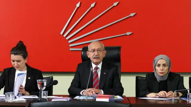 Kemal Kılıçdaroğlu ortada duruyor. Sol yanında başörtülü bir üye var, diğer tarafında ise başı açık bir kadın elindeki dosyaya baklıyor.