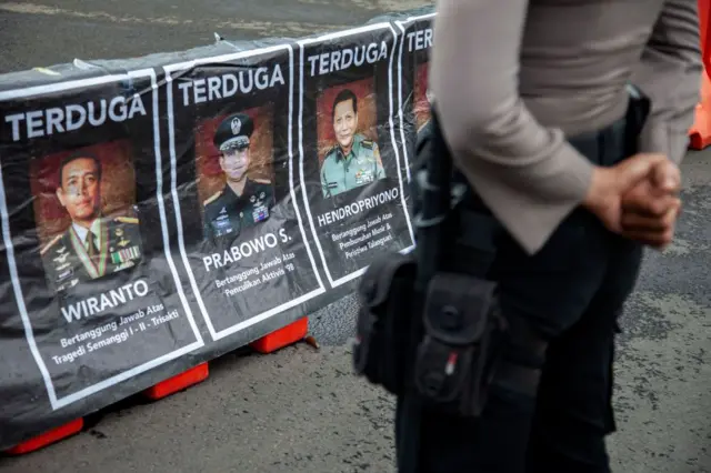 Seorang petugas polisi berjaga di depan poster yang memajang foto tersangka penculikan para aktivis pada 1997/1998, sementara aktivis hak asasi manusia menggelar unjuk rasa yang dikenal sebagai Aksi Kamisan di depan Istana Negara di Jakarta, pada 29 Februari 2024.