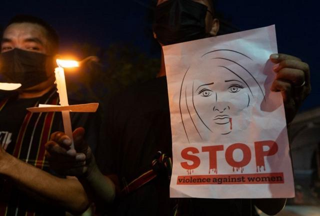 Une femme avec une bougie allumée et une banderole disant : "Stop à la violence contre les femmes".