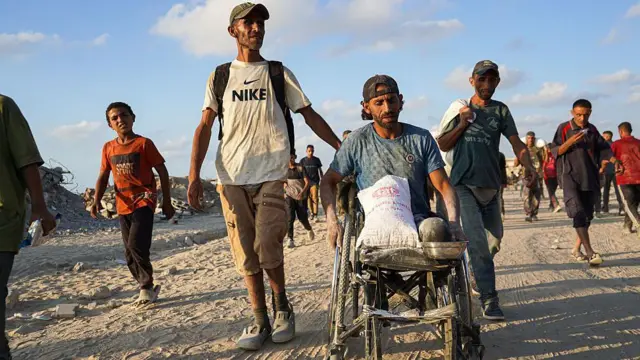 A man in a wheel chair surrounded by other men leaves an aid station after collecting food aid in Gaza