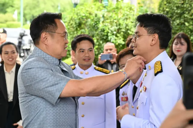 นายกฯ จัดเสื้อให้นายไชยชนก ชิดชอบ รมต.ดีอีเอส วัย 35 ปี บุตรชายของนายเนวิน ชิดชอบ จนถูกผู้สื่อข่าวแซวว่าทำหน้าที่แทนพ่อ ก่อนที่นายกฯ จะหัวเราะพลางพูดว่า "อา ๆ"