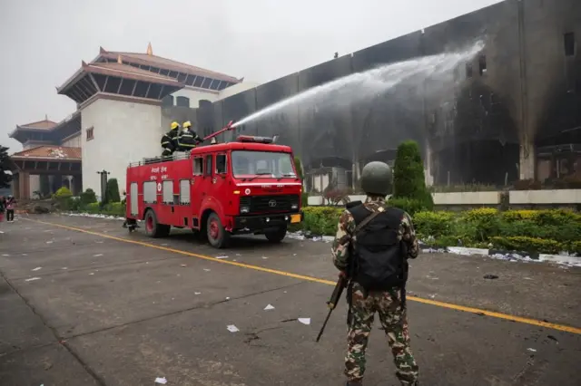 संसद् भवनमा लागेको आगो निभाउँदै एउटा दमकल, अगाडि एक सैनिक उभिएका छन्