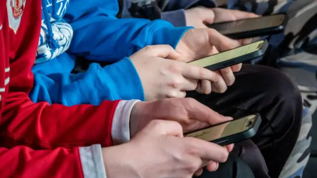 Un grupo de jóvenes mira a sus teléfonos celulares. 