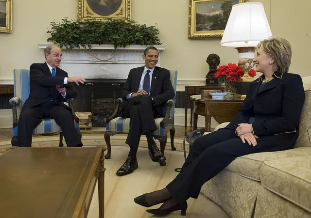 George Mitchell, Barack Obama ve Hillary Clinton Oval Ofis'te oturuyor, hepsi gülüyor.