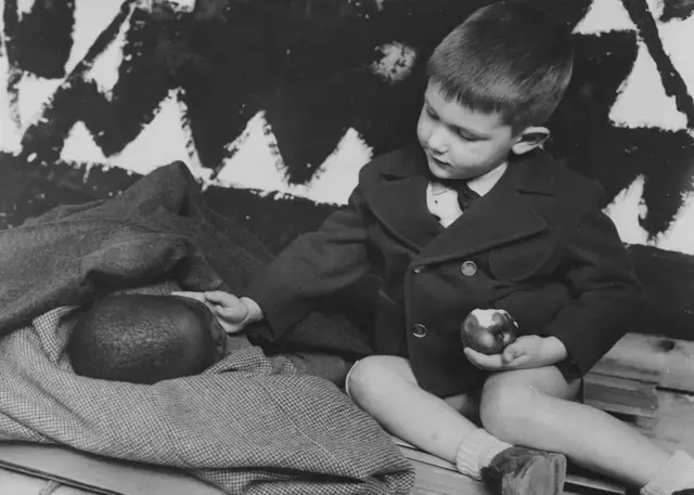 Un enfant blanc assis à côté d'un enfant noir couché.