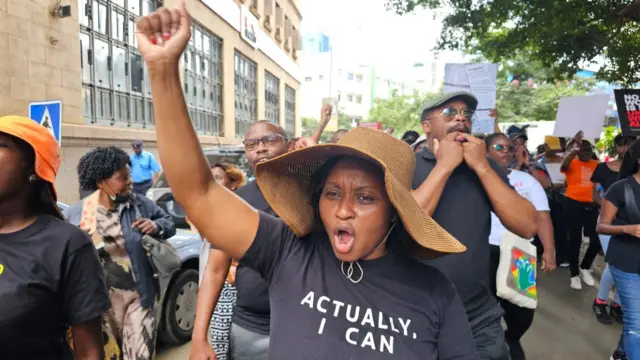 Umugore ari mu myiyerekano akiriza ikiganza akoma akaruru muri iyo myiyerekano